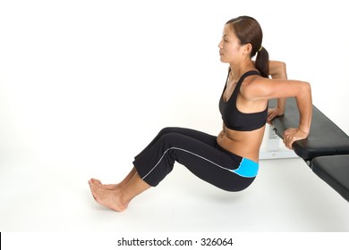 A female fitness instructor demonstrates the finishing position of the tricep bench dips