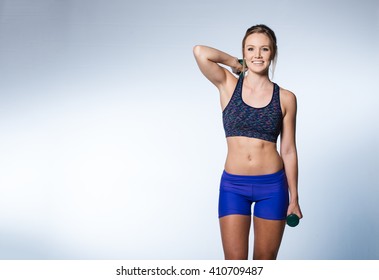 Female fitness model excercising in studio with dunbell weights and doing a floor routine of stretches and lifts on a matt.