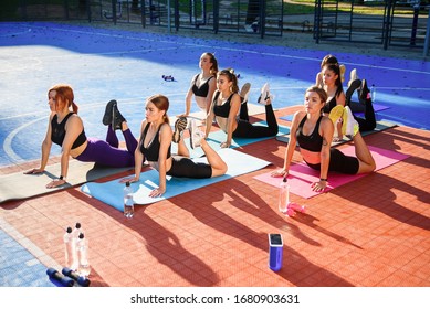 Female Fitness Team Of Attractive Slender Girls Doing Yoga Exercises On Special Mats On The Outdoor Stadium In The Urban Park. Healthcare And Active, Sports Lifestyle Concept.