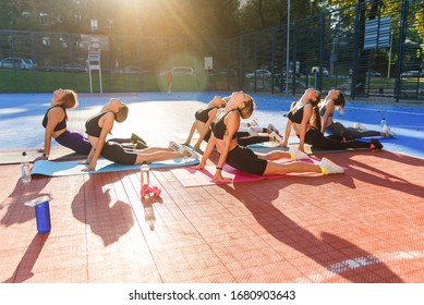 Female Fitness Team Of Attractive Slender Girls Doing Yoga Exercises On Special Mats On The Outdoor Stadium In The Urban Park. Healthcare And Active, Sports Lifestyle Concept.