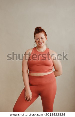 Female in fitness wear standing after workout. Fit plus size woman looking at camera and smiling.