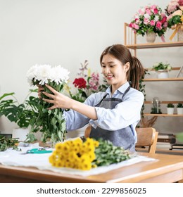 Female florist in apron holding white chrysanthemum to creating and designing floral for arrangement flower bouquet on the table in her flower shop. - Powered by Shutterstock