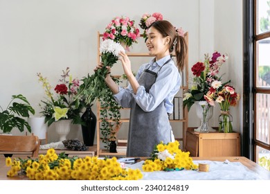 Female florist in apron holding white chrysanthemum with enjoying to creating and designing floral for arrangement flower bouquet on the table in her flower shop. - Powered by Shutterstock