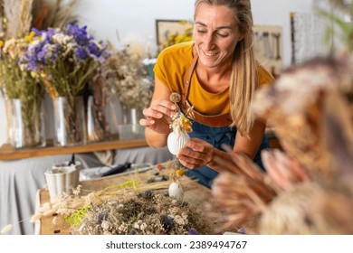 female florist arranging a small white vase with dried flowers in a bright workshop - Powered by Shutterstock