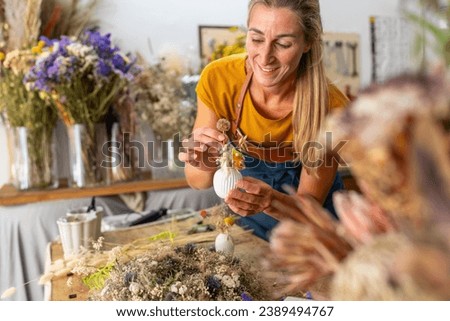 female florist arranging a small white vase with dried flowers in a bright workshop