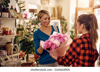 Female florist giving her customer bouquet of flowers at flower shop. Focus is on customer.  - Powered by Shutterstock