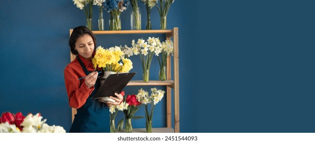 A female florist holds a bouquet and makes notes on a clipboard while standing in her flower shop. Small business and floristry concept. Banner. Copy space - Powered by Shutterstock