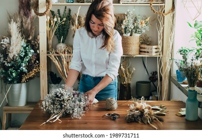 Female Florist Making Everlasting Bouquet Of Dried Flowers At Wooden Table In Her Workshop 
Young Woman Entrepreneur Running Her Small Business With Dry Plants And Flowers At Rustic Store.