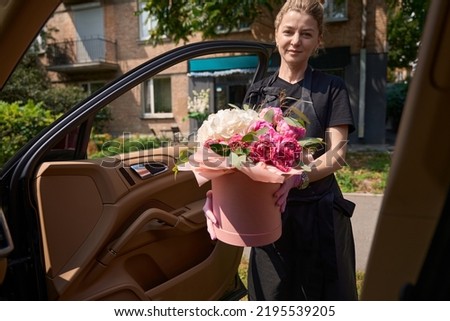 Female florist opened side door of car to give luxurious bouquet of flowers