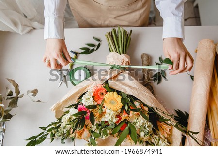 a female florist ties a ribbon bow on a bouquet of flowers wrapped in craft paper on the desktop. Top view. High quality photo