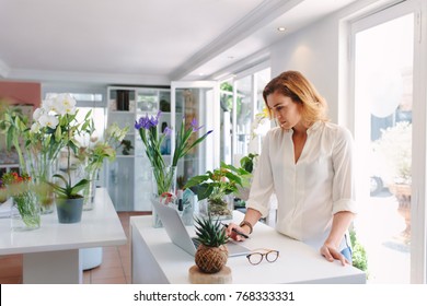 Female Florist Using Laptop At Counter In Plant Nursery.  Small Flower Shop Owner Working On Laptop In Her Shop.