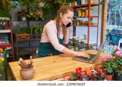 Female Florist Using Smartphone And Laptop Computer In Flower Shop Online Taking Order