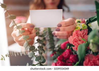 Female florist at work: pretty young dark-haired woman making fashion modern bouquet of different flowers. Women working with flowers in workshop. She is holding a business card. - Powered by Shutterstock