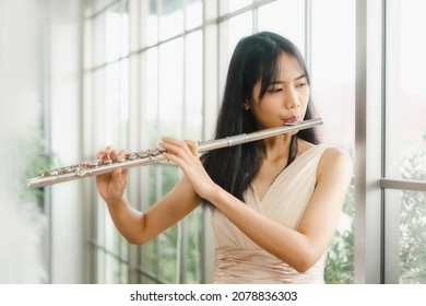 A Female Flutist Performs On Her Instrument. A Young And Elegant Asian Woman Plays The Flute