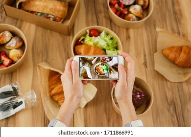 Female Food Blogger Reviewing Takeout Food, Taking Video On Phone. Italian Sub Sandwich, French Croissant W/ Salmon, Chocolate Cheesecake. Close Up, Top View, Pov, Copy Space, Wooden Table Background.