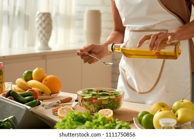 Female food blogger wearing apron pouring olive oil into vegetable salad while standing at modern kitchen, close-up shot - Powered by Shutterstock