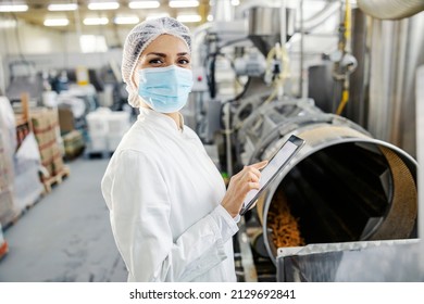 A Female Food Factory Inspector Touching Tablet And Checking On Snacks Quality During Covid 19.