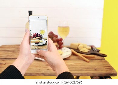 Female food photographer with mobile phone taking picture of cheese and wine