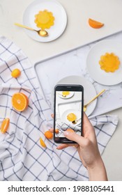 Female Food Photographer With Mobile Phone Taking Picture Of Tasty Orange Jelly, Top View