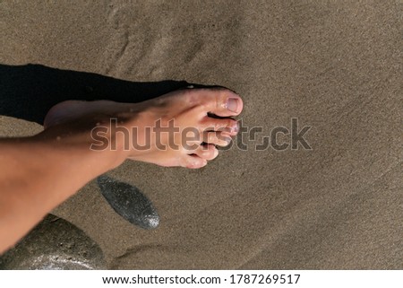 female foot stands on the wet sand of a pacific beach