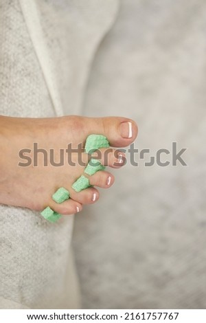 female foot with toe separator in green color, on a light background, pedicure in a beauty salon, close-up