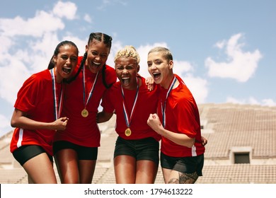 Female Football Team Celebrating The Victory At Stadium. Woman Soccer Players With Medals Shouting In Joy After Winning The Championship.