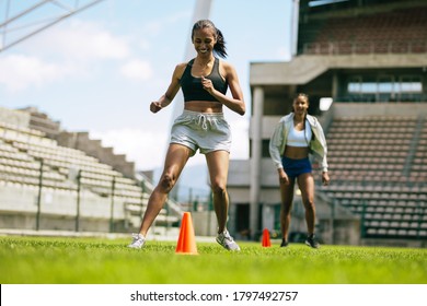 Female footballers practicing ball control by dribbling around orange cones on the field. Female footballers improving agility with running drills. - Powered by Shutterstock