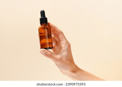 Female fragile hand holding transparent glass jar of face serum with dispenser on beige isolated background. The concept of moisturizing and nourishing the skin, beauty products - Powered by Shutterstock