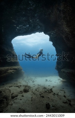 A female free diver poses in front of an underwater cave opening in the clear blue waters of Hawaii. Model release provided.