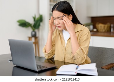 Female freelance with eyes closed is massaging head temples with suffering face expression. Tired and worn out from online work young woman sitting in front laptop holding head, feels strong headache