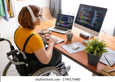 Female freelance programmer in modern headphones sitting in wheelchair and using computers while coding web game at home - Powered by Shutterstock