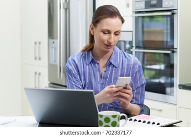 Female Freelance Worker Using Laptop In Kitchen At Home