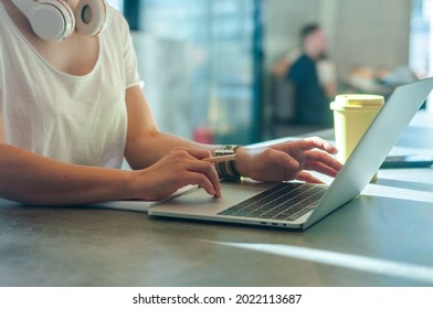 Female freelancer wearing headphones working on the laptop and drinking coffee. Generation Z concept. - Shutterstock ID 2022113687