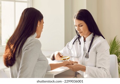 Female friendly doctor examining hand skin of young woman patient. Professional dermatologist using magnifying glass checking skin condition in clinic. Dermatology, skin health care concept. - Powered by Shutterstock