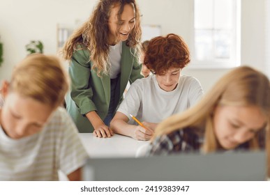 Female friendly woman teacher helping a boy during a lesson in the classroom in junior high school. Schoolchildren sitting at the desks and working. Education, knowledge and back to school concept. - Powered by Shutterstock