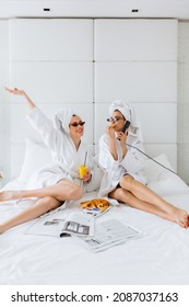 Female Friends In Bathrobe Having Fun In Bed At Hotel. Breakfast In Bed