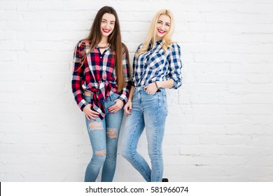 Female friends in checkered shirts and jeans standing together on the white wall background