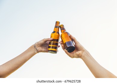 Female Friends Cheers Clinking Bottles Of Beer In Hands In The Park.