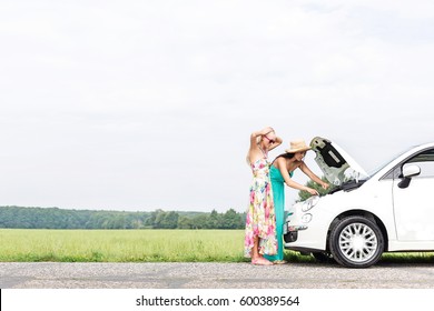 Female friends examining broken down car on country road against clear sky - Powered by Shutterstock