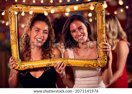 Female Friends Having Fun Posing With Photo Booth Photo Frame At Party In Bar