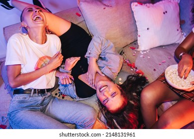 Female friends laughing hysterically at a house party. Three happy young women having a good time while chilling together on a couch. Friends enjoying a girls night during the weekend.
