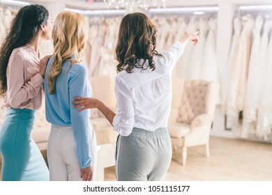 Female Friends Looking At Dresses In Wedding Fashion Shop