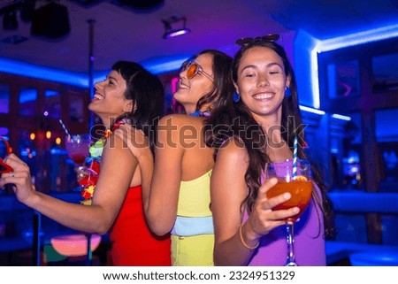 Female friends in a nightclub drinking glasses of alcohol smiling at a night party