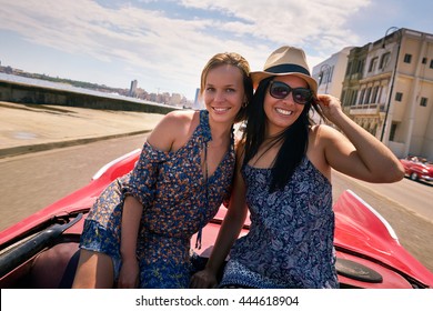 Female Friends On Holidays, People Traveling, Young Women Having Fun On Vacation, Two Happy Girls Smiling In Havana, Cuba. Hispanic Persons Laughing On Old Classic Convertible Car. Slow Motion