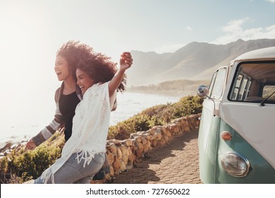 Female Friends On Road Trip Enjoying Outdoors On A Sunny Day. Women Standing Outside Van  And Laughing.