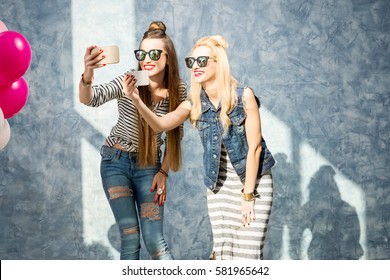Female friends photographing with phones standing on the blue wall background