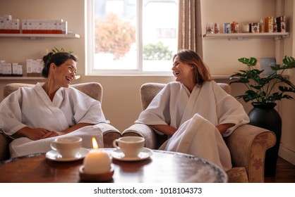 Female Friends Sitting In Reception Area And Talking Before Spa Treatment. Two Young Women Relaxing In Beauty Spa Waiting Room And Smiling.