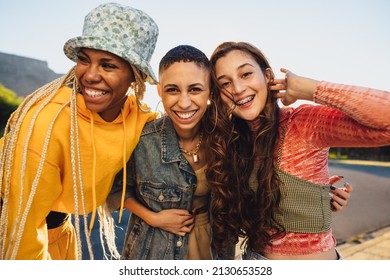 Female friends smiling cheerfully while embracing each other. Female youngsters having fun while standing together outdoors. Group of generation z friends making happy memories together. - Shutterstock ID 2130653528