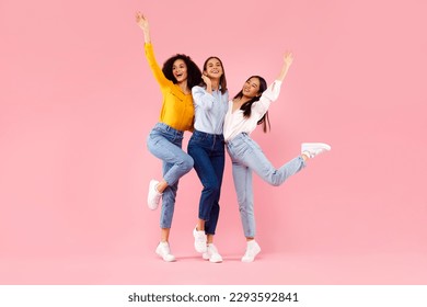 Female friendship concept. Joyful diverse ladies embracing and having fun, smiling at camera, friends posing together over pink studio background, full length, free space