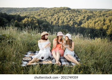 Female Friendship. Picnic Time. Three Attractive Girls Having Fun And Enjoying Picnic Lunch, Against The Background Of Green Hills. Blanket With Food Spread On It.